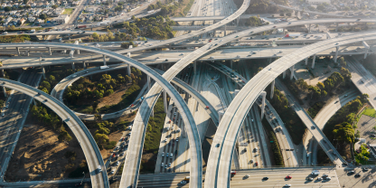 Aerial view of a complex highway interchange with multiple overpasses and lanes of traffic, surrounded by greenery and urban development.